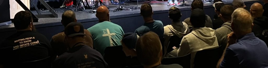 A room of men seated, seen from behind