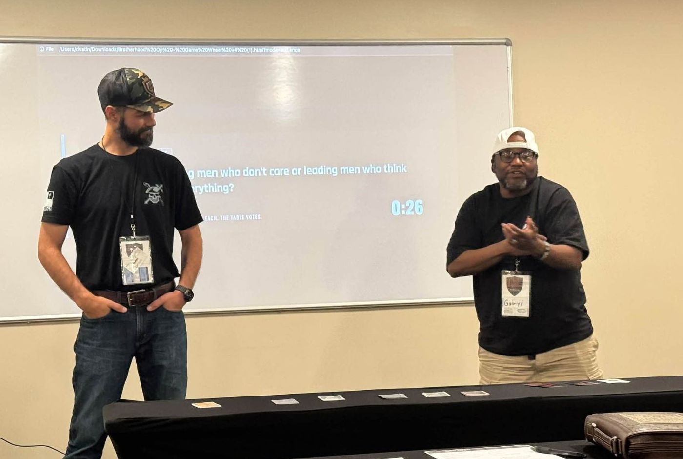 Two men running a round of the game in front of a room